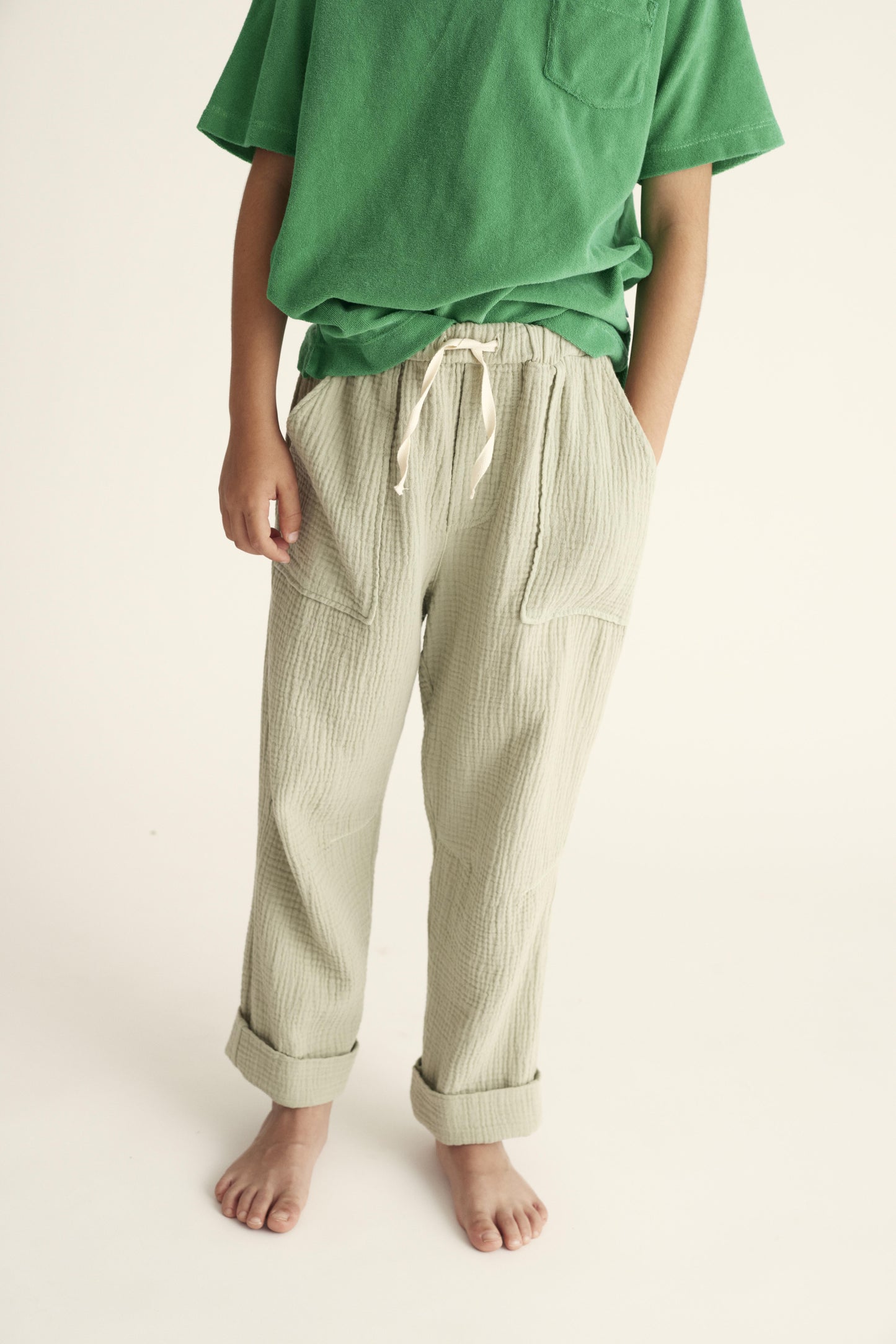 Kind trägt die Iker Hosen von Cozmo in Grün, mit lockerer Passform und atmungsaktivem Musselin-Material.