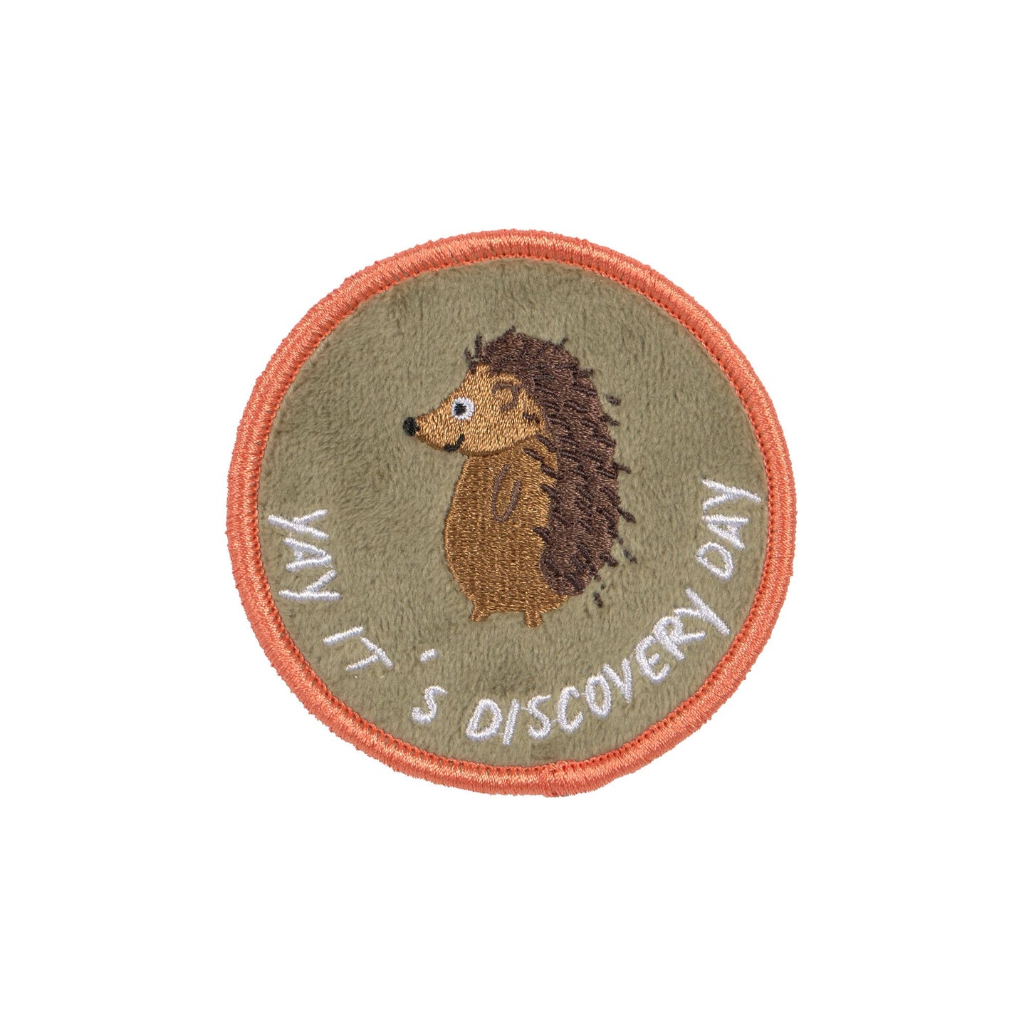 Runde Patch mit Igel-Motiv auf olivgrünem Hintergrund, umrahmt von einer orangefarbenen Stickerei und der Aufschrift "Yay, It's Discovery Day".