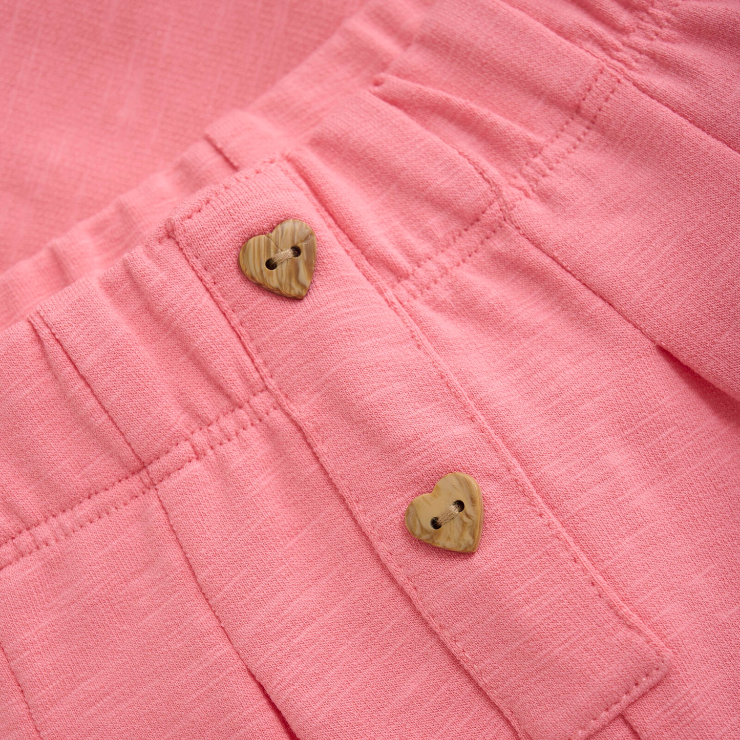 Nahaufnahme der Baby-Sweathose in Erdbeer-Pink, weicher Baumwollstoff mit hübschen Holzknöpfen