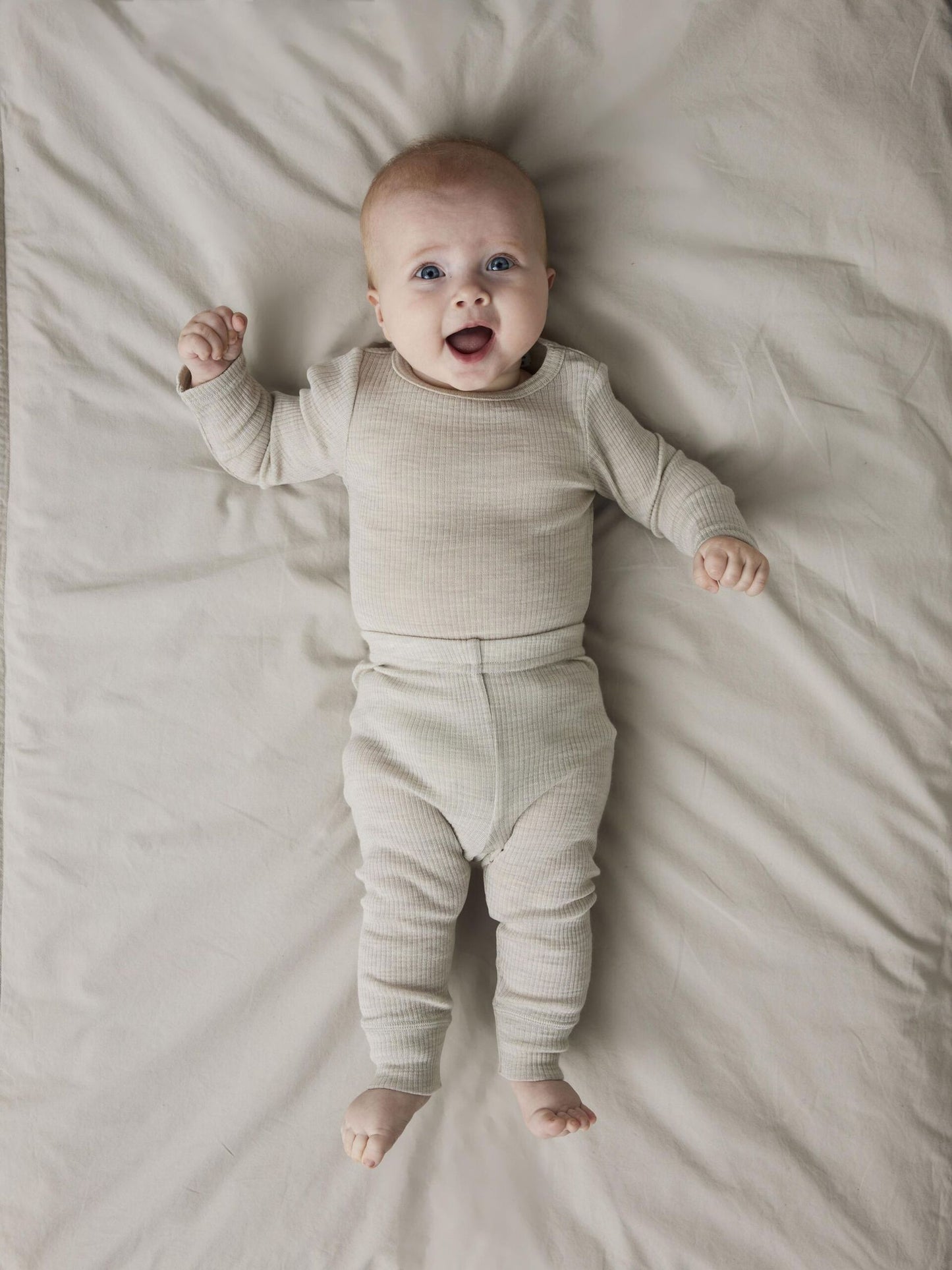 Baby liegt auf Bett und trägt graue gerippte Merinowoll-Leggings