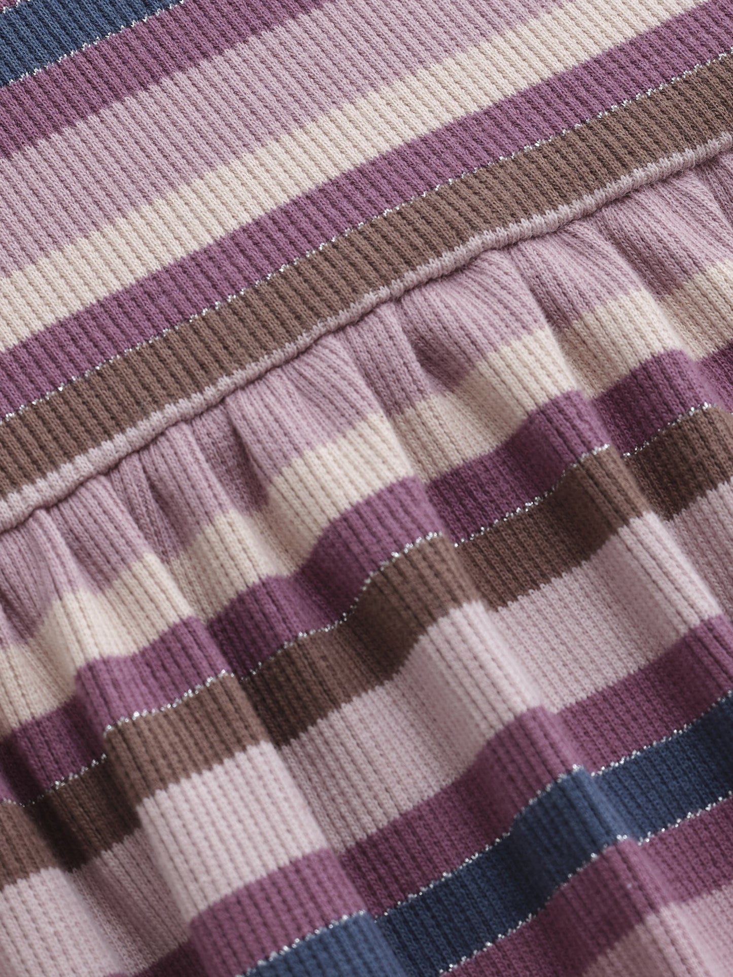 Detailaufnahme vom gestreiften Stoff des Kinderkleids in Lila-, Rosa- und Beigetönen.