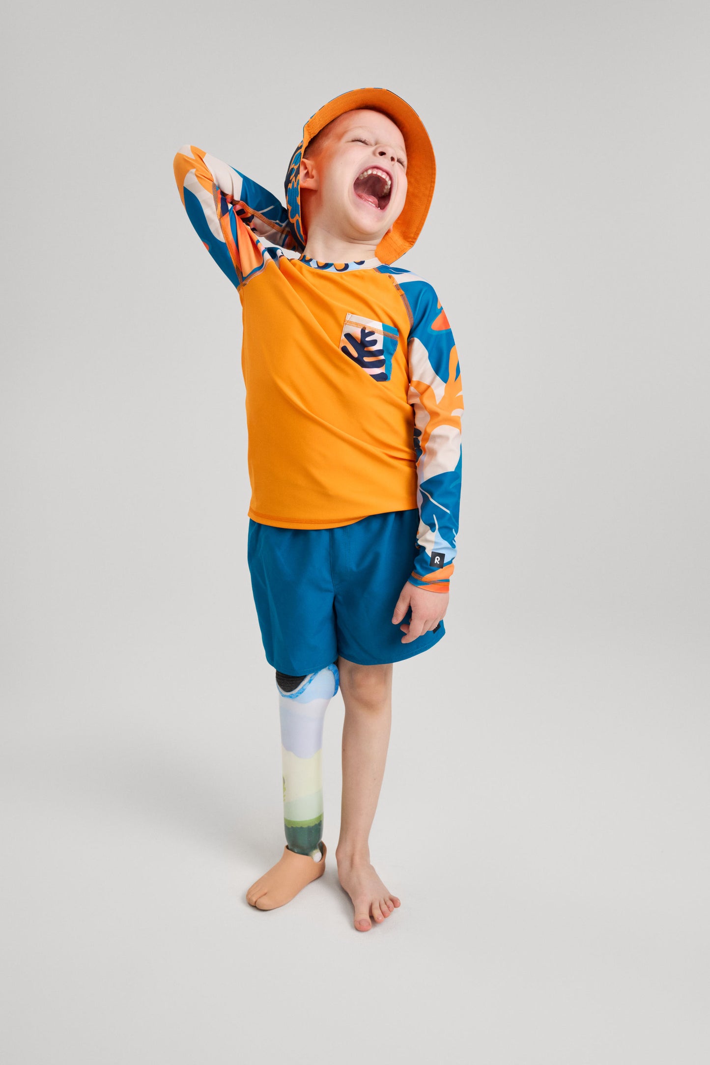 Kind trägt orangefarbenes Reima UV-Schwimmshirt mit Brusttasche von Kroolaus, kombiniert mit blauer Badehose, ideal für Strand und Sonne. Zu kaufen im Bärechind in Winterthur, Zürich, Schweiz.