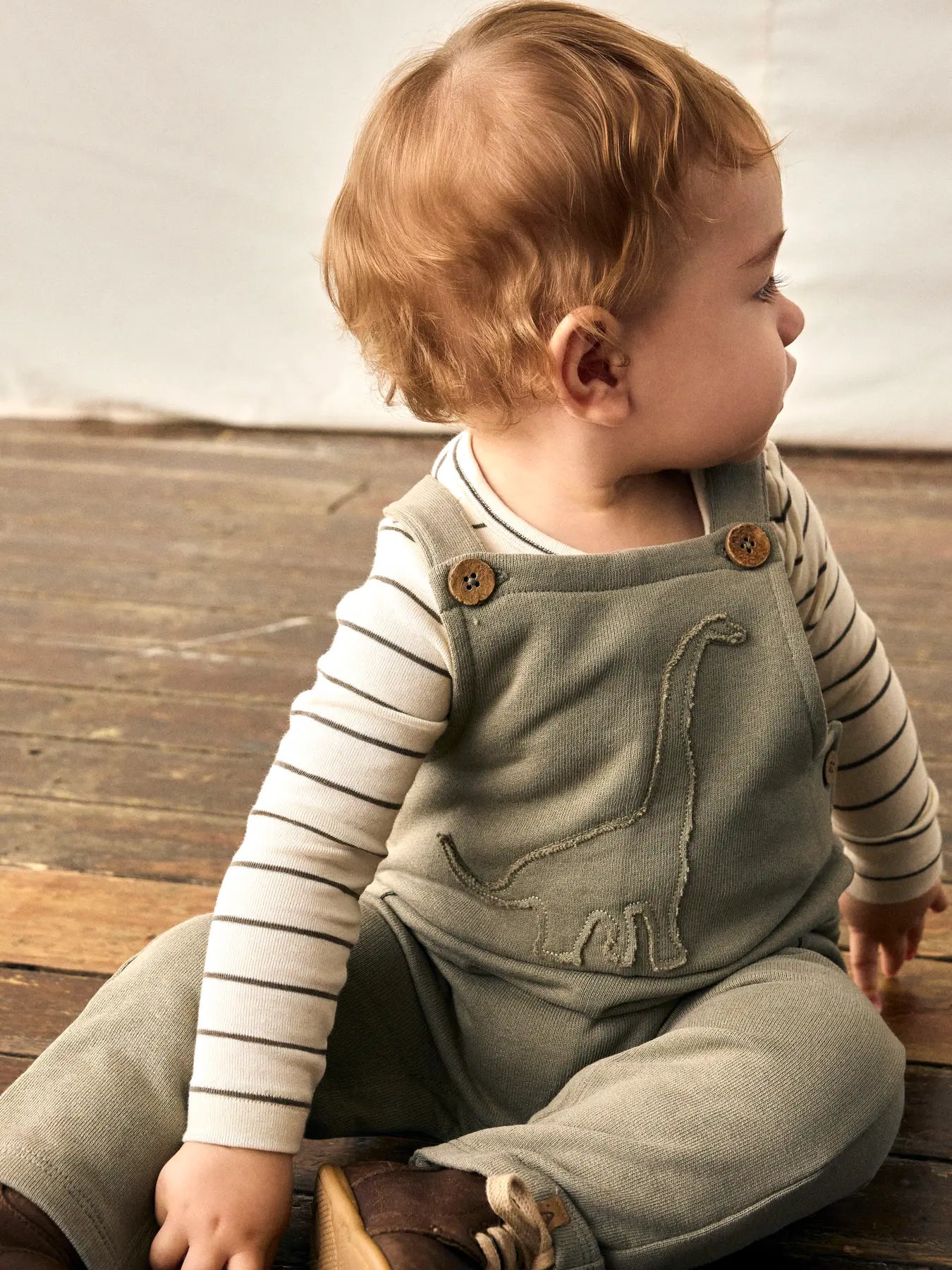 Baby trägt Lil' Atelier Latzhose mit Dino-Stickerei aus Bio-Baumwolle – erhältlich bei Bärechind Winterthur.