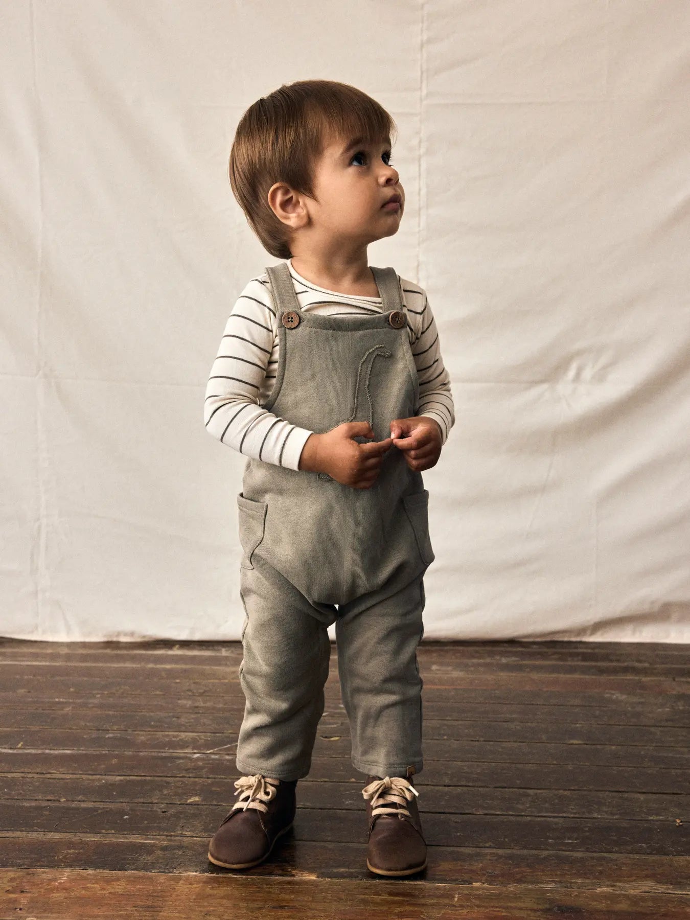 Kind trägt Dino-Latzhose von Lil' Atelier aus Bio-Baumwolle – fair & verspielt, erhältlich bei Bärechind Winterthur.