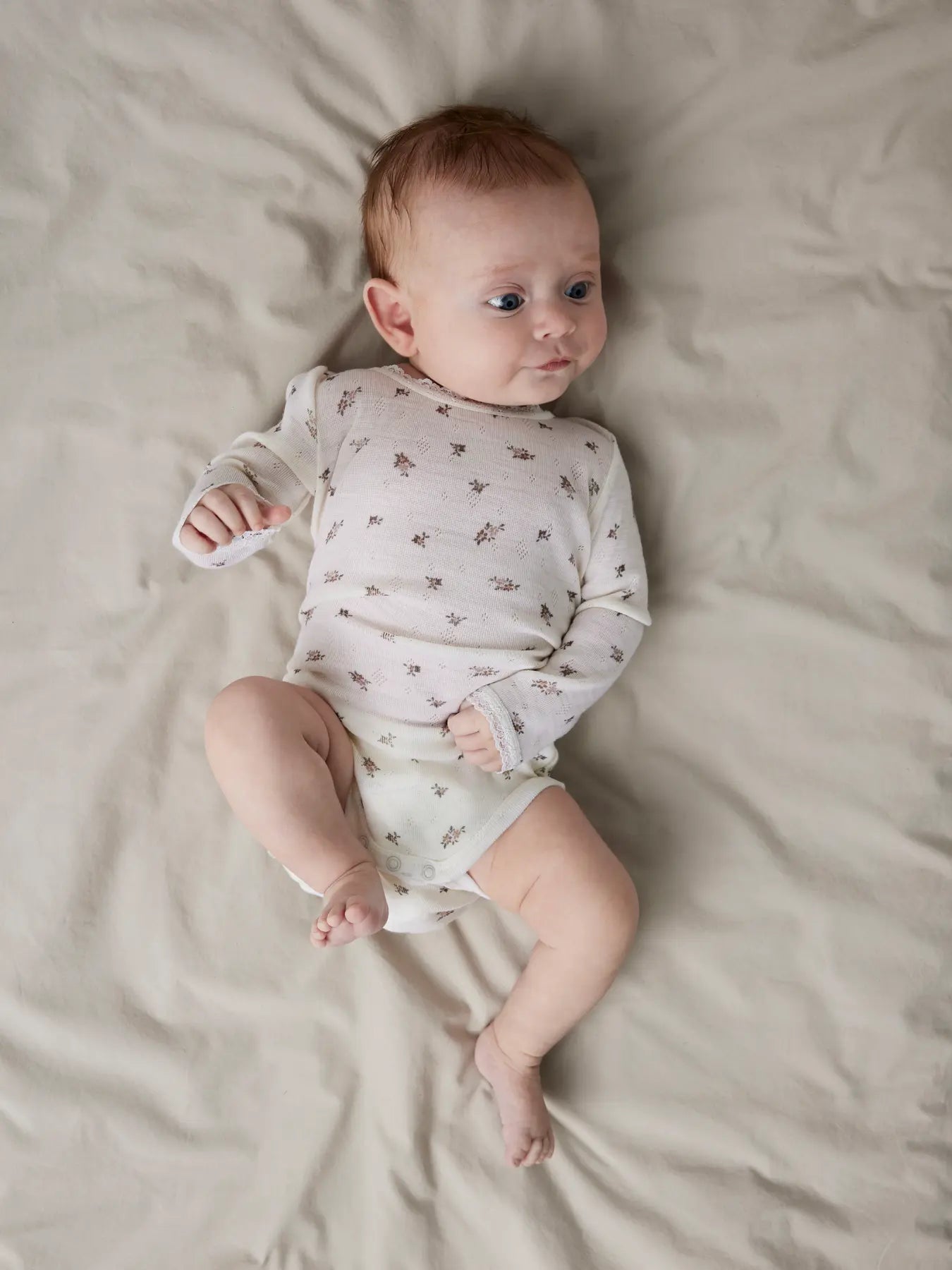 Ein Baby trägt den Lil’Atelier Merino-Body mit Blumenmuster in Winterthur.