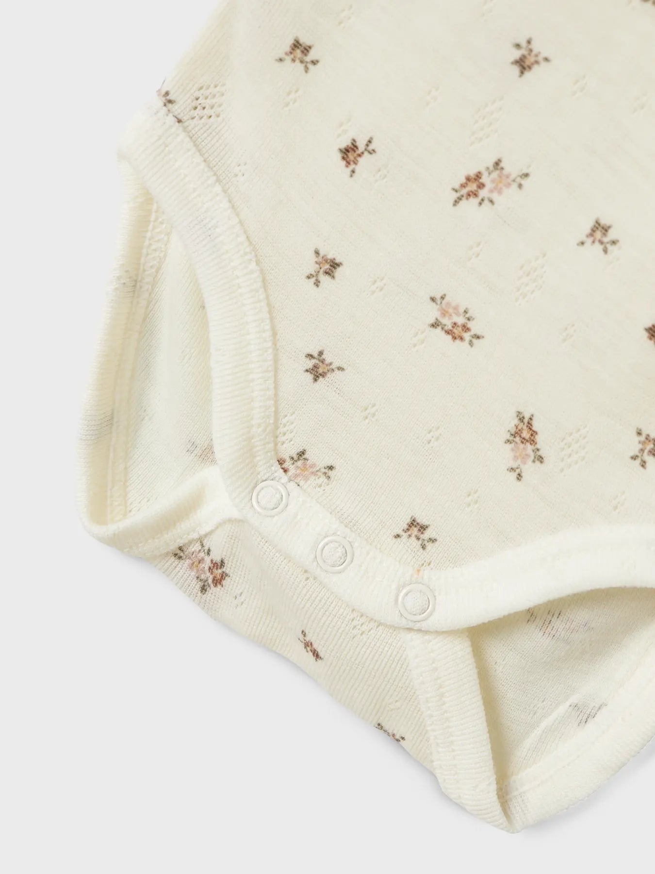Detailaufnahme vom Knopfbereich des Lil’Atelier Merino-Bodys mit zartem Blumenmuster, erhältlich in Winterthur.