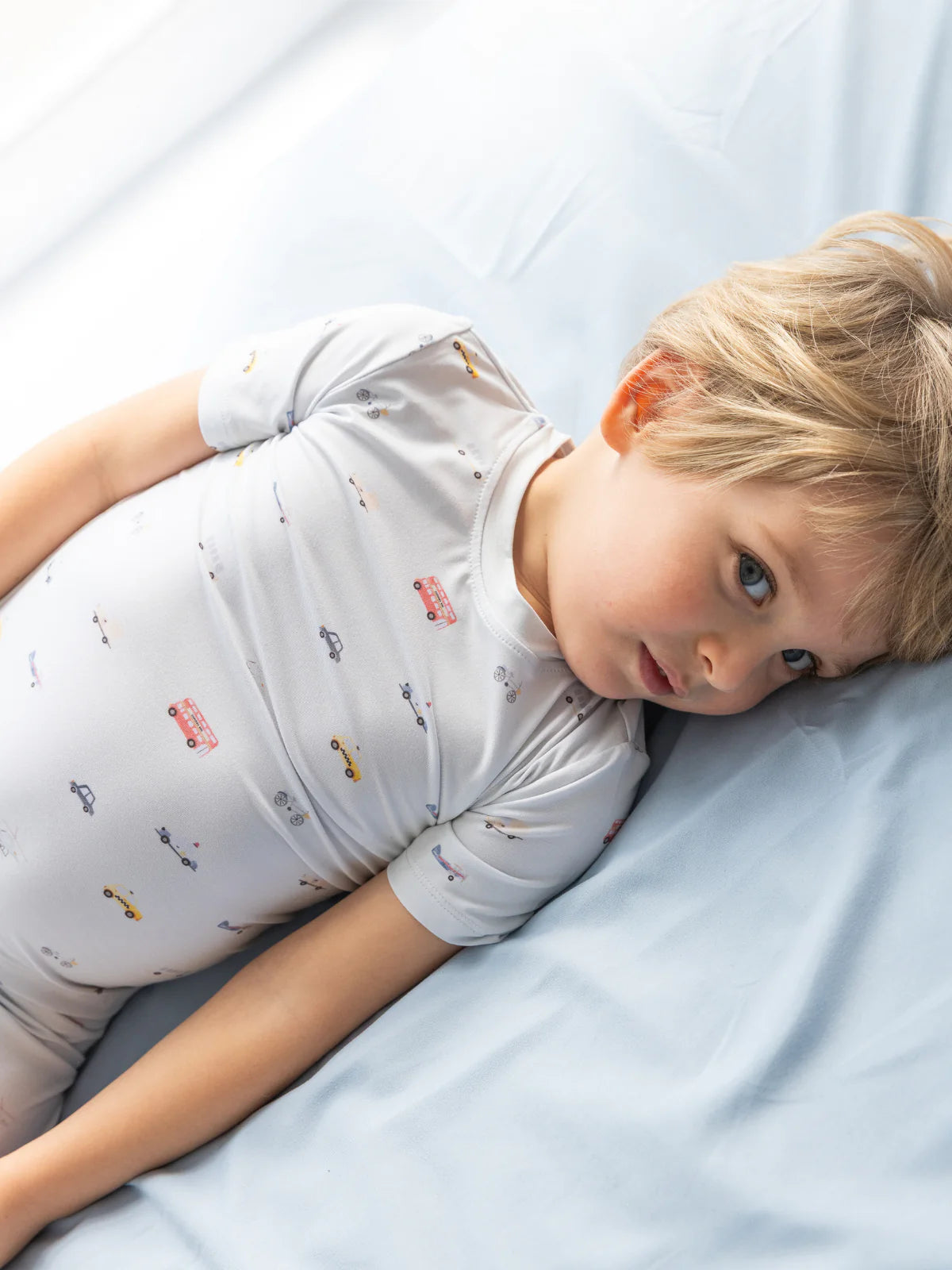 Kleinkind liegt entspannt im Bett mit dem kurzärmligen Bambus-Schlafanzug Little Ride – weich, atmungsaktiv & kindgerecht.
