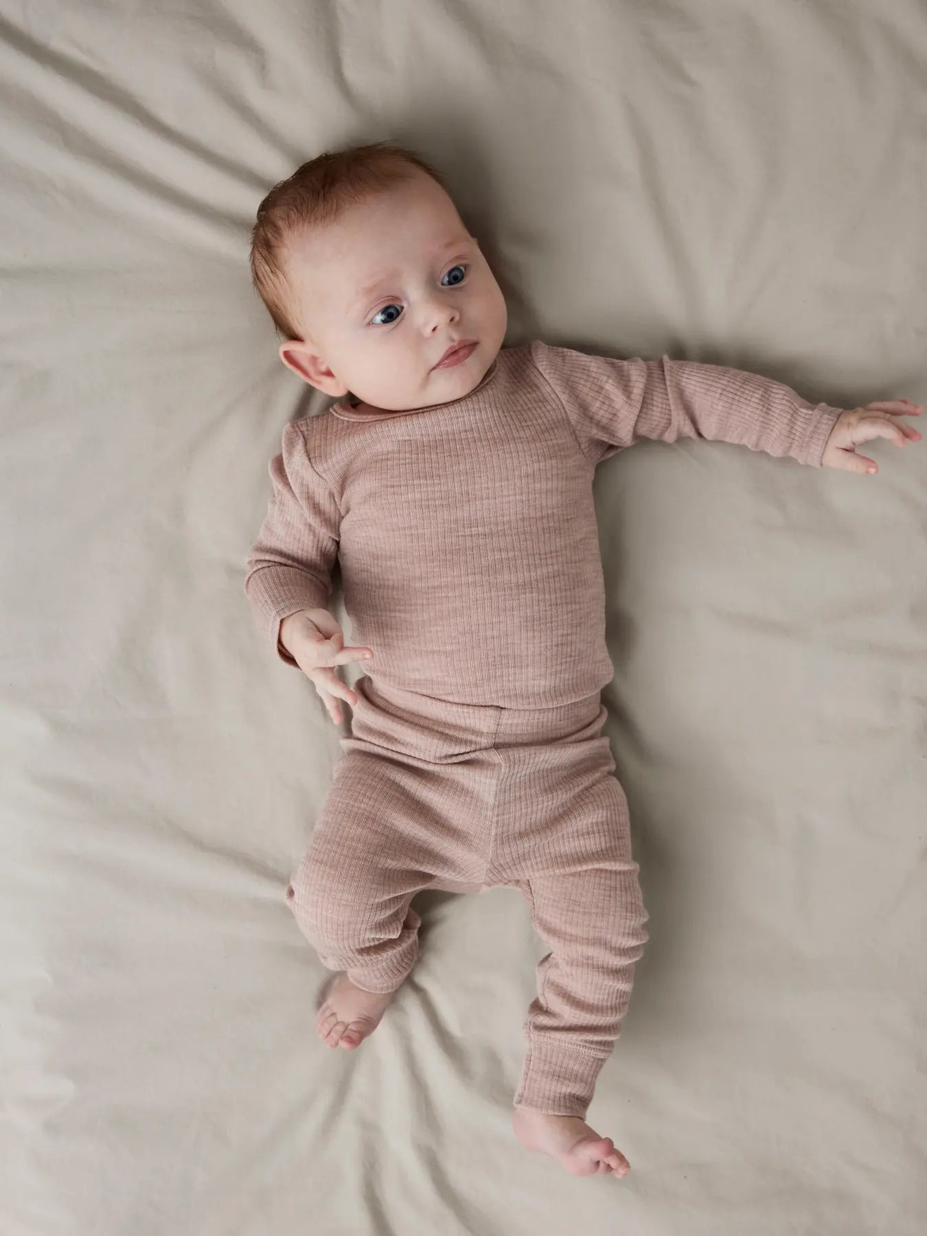 Baby liegt in altrosa Wollleggings auf dem Bett – erhältlich bei Bärechind in Winterthur, Zürich, Schweiz.