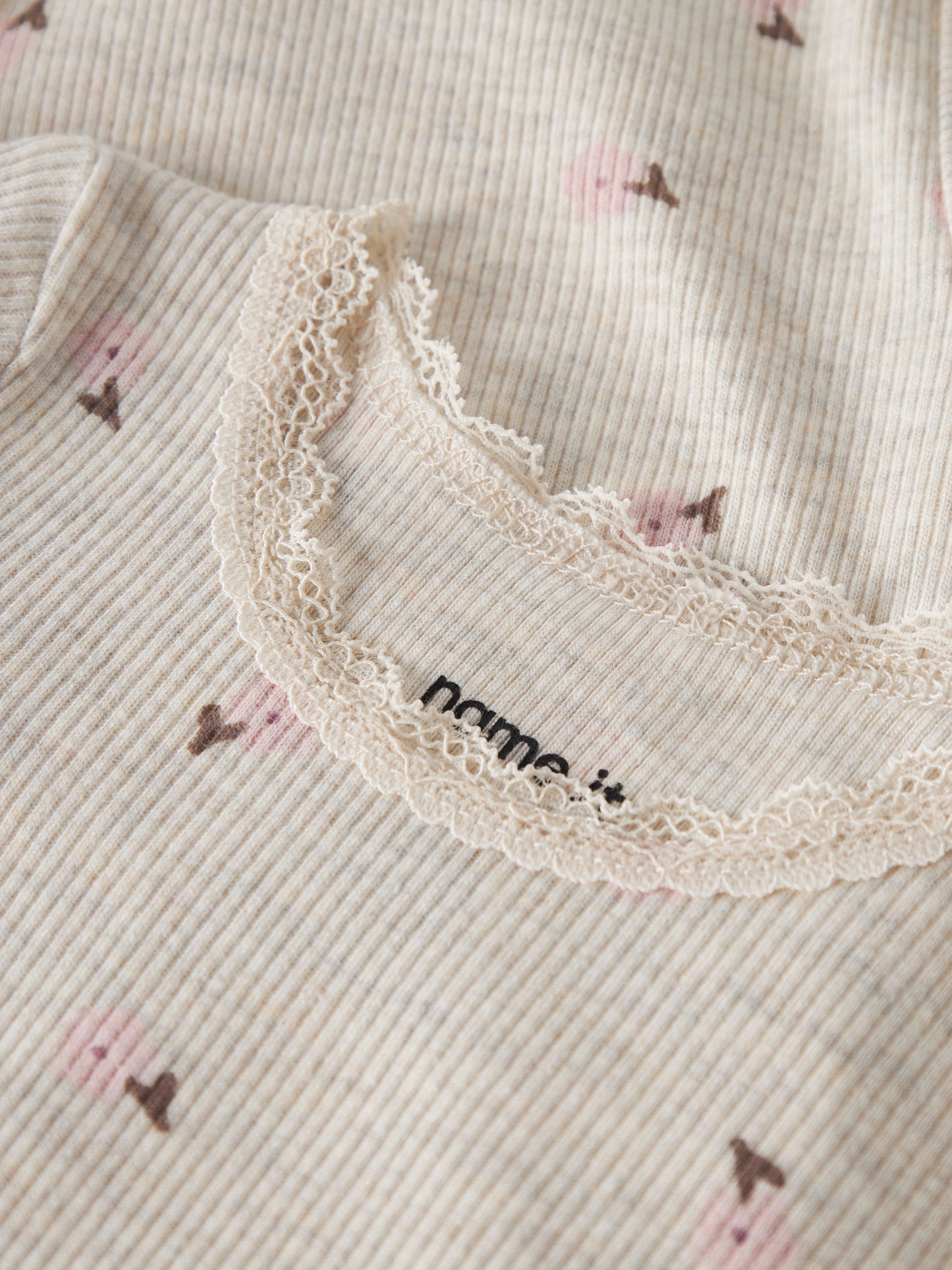 Detailaufnahme des NAME IT Ripp Bodys aus Baumwolle und TENCEL™ Lyocell in Creme mit rosa Blumenprint und feiner Spitzenkante, erhältlich im Bärechind Winterthur.