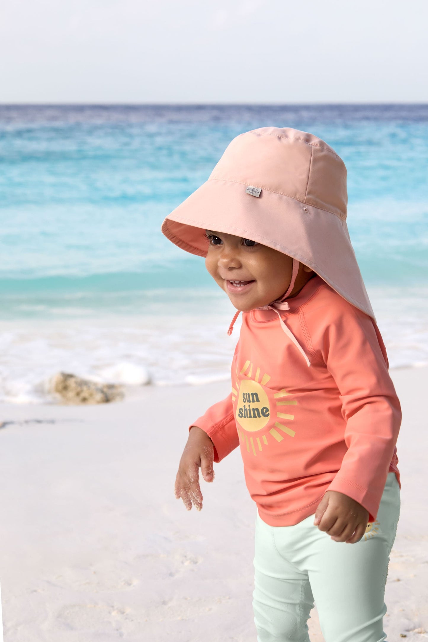 Kind in LÄSSIG UV-Shirt mit Sonnenhut am Strand – nachhaltig & sicher bei Bärechind in Winterthur, Zürich, Schweiz kaufen.