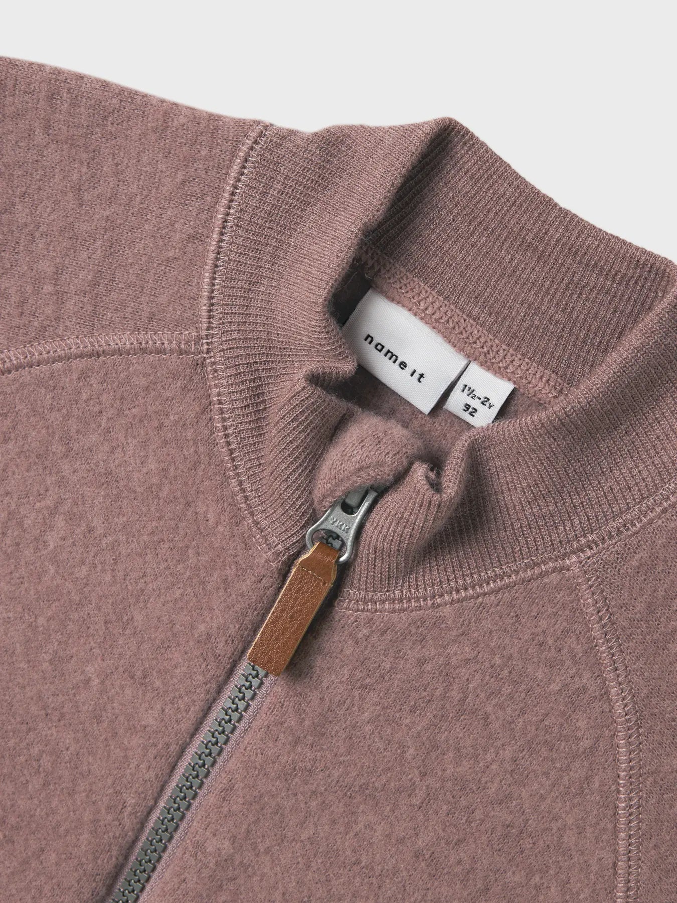 Nahaufnahme vom Reissverschluss und Kragen eines rosa Wollfleece-Jäckchens für Kinder.