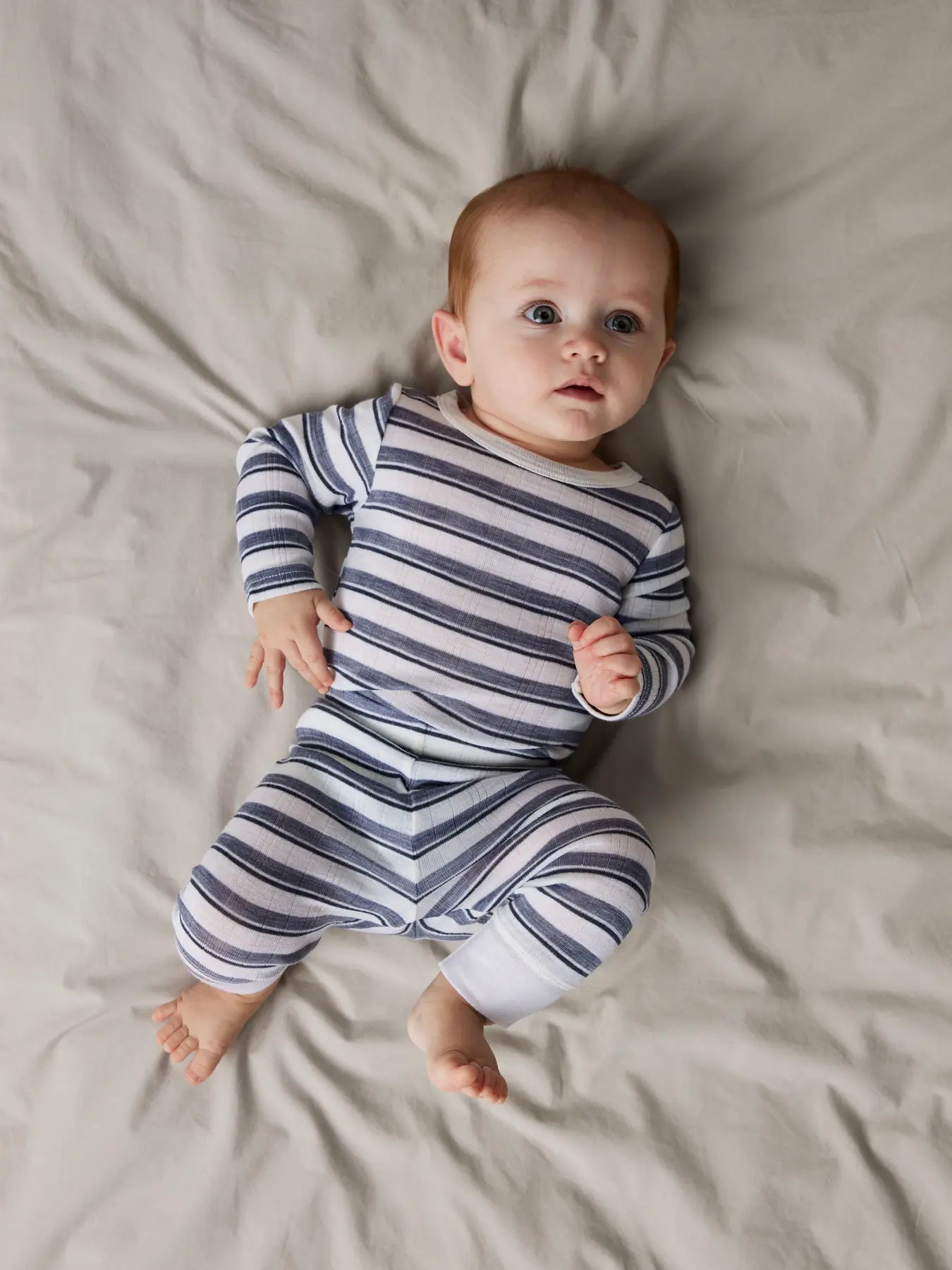 Baby trägt gestreifte Wollleggings von NAME IT auf Bett – erhältlich bei Bärechind in Winterthur, Zürich Schweiz.