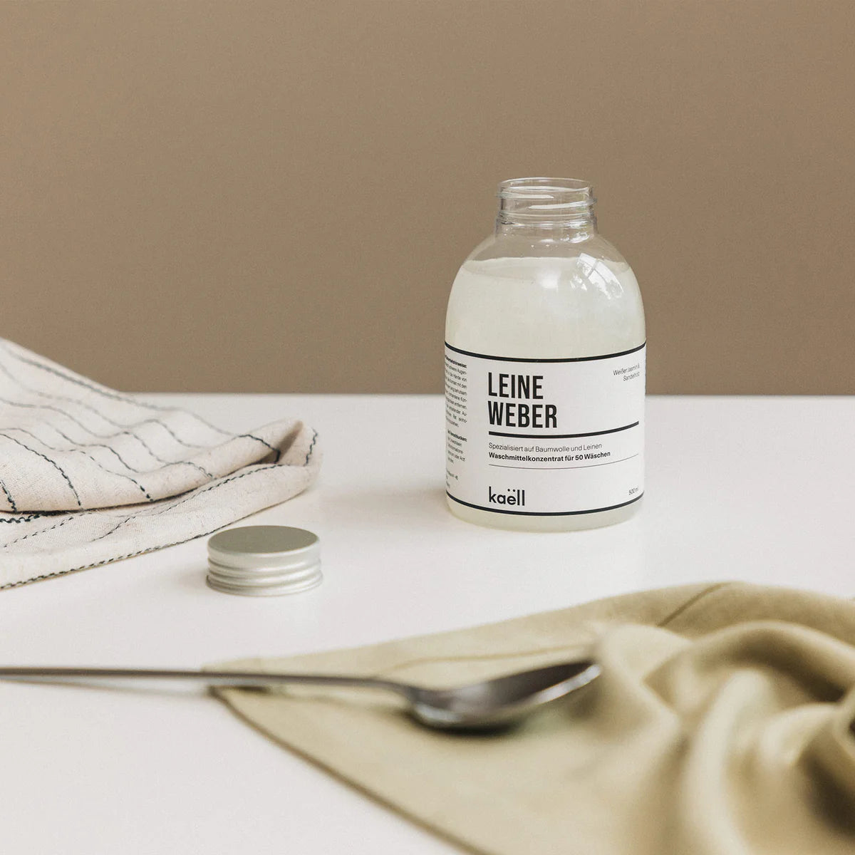 500 ml Leineweber Waschkonzentrat neben weichem Stoff aus Baumwolle und Leinen. Hochwertige Pflege für Naturfasern, mit sanfter, hautfreundlicher Formel und edlem Duft.