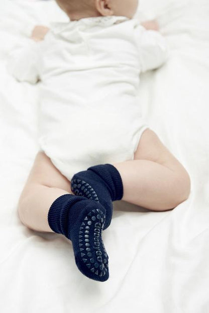 Baby mit navyfarbenen GoBabyGo Anti-Rutsch-Socken aus Bambus auf weichem Untergrund