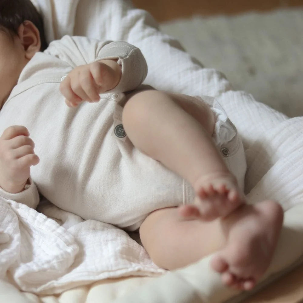 Baby trägt den beigen Merino Wickelbody von Emma & Noah als weiche erste Kleidungsschicht.