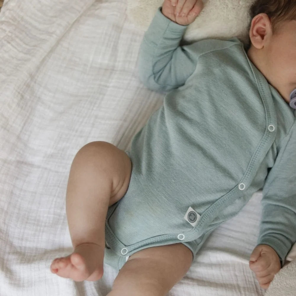Mintfarbener Emma & Noah Merino Wickelbody am Baby mit sichtbarer Wickelöffnung und Druckknöpfen, erhältlich im Bärechind in Winterthur