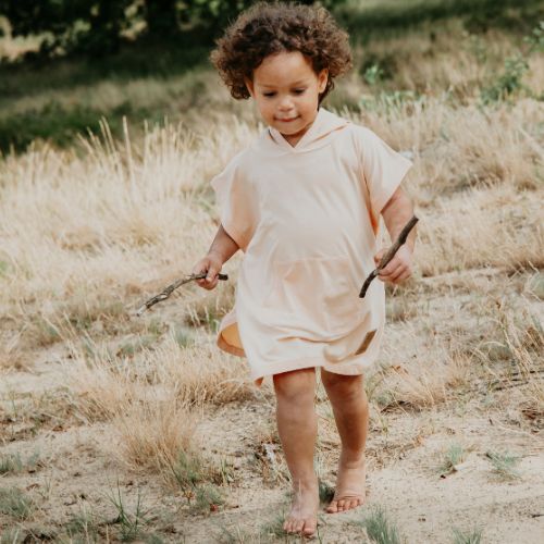 Kind trägt Cloby UV-Poncho in Peachy mit Kapuze und Vordertasche – Leichter Poncho mit UPF 50+ Schutz. Perfekt für Strand, Spielplatz und Alltag. Jetzt in Winterthur, Zürich, Schweiz erhältlich.