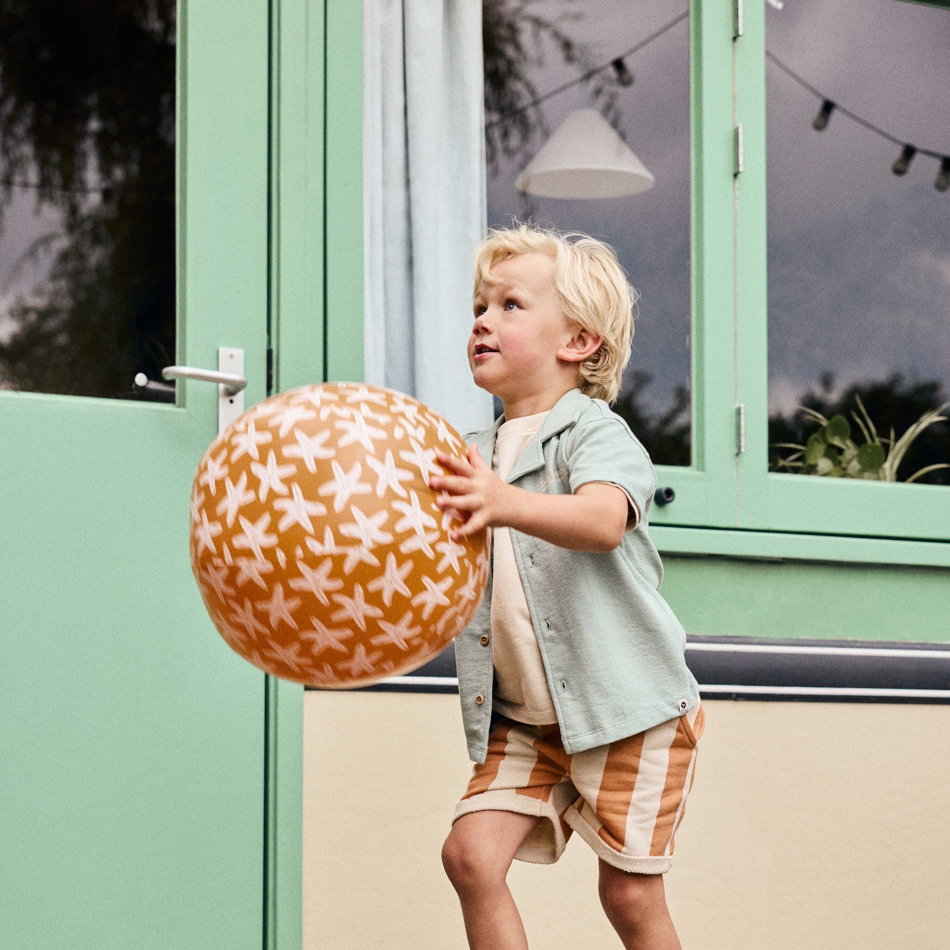 Kind trägt Daily7Kids Shorts mit Streifen in Apricot – bequeme Sommer Kindermode