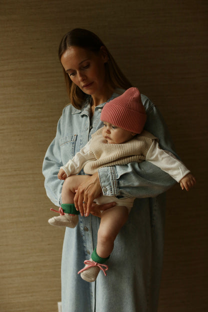 Mutter trägt Baby in den Hvid Strickschuhe Booties in Cream/Grass auf dem Arm