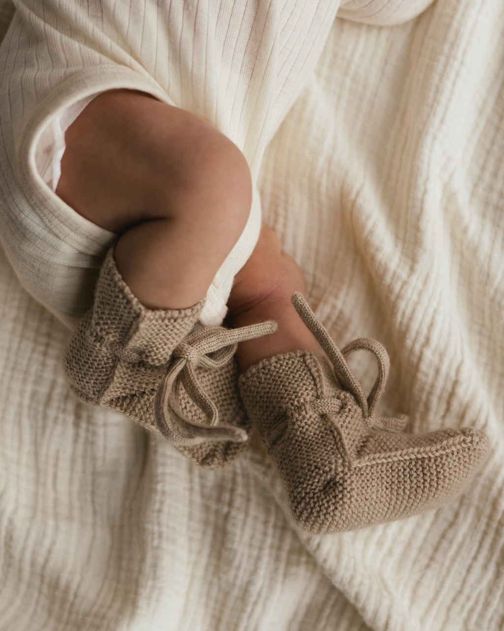 Baby trägt die Hvid Strickschuhe Booties in Sand, erhältlich bei Bärechind