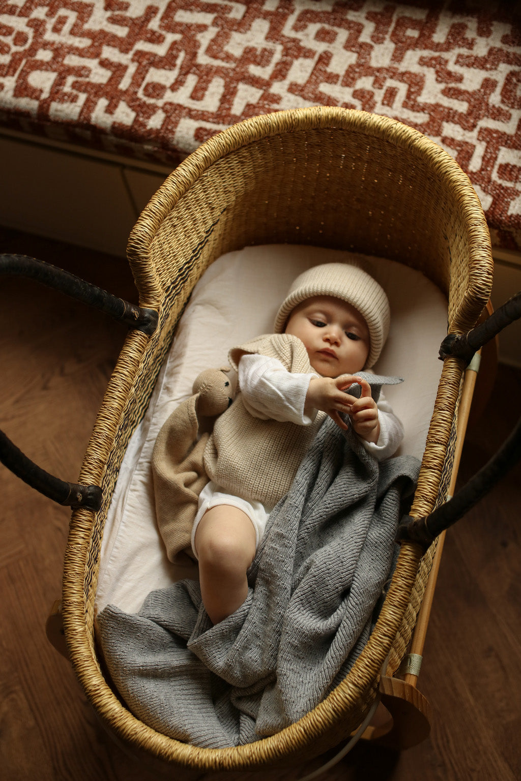Baby in der Hvid Strickweste Harvey in Sand liegt im Stubenwagen