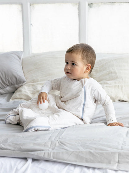 Baby trägt den LiluLila Karo Bambus Schlafsack auf dem Bett. Nachhaltig, hypoallergen und Oeko-Tex zertifiziert. Perfekt für empfindliche Haut. Erhältlich im Kinderladen in Winterthur, Zürich, Schweiz.