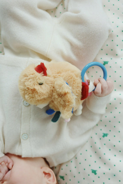 Baby hält Peluche Mio in der Hand beim Kuscheln