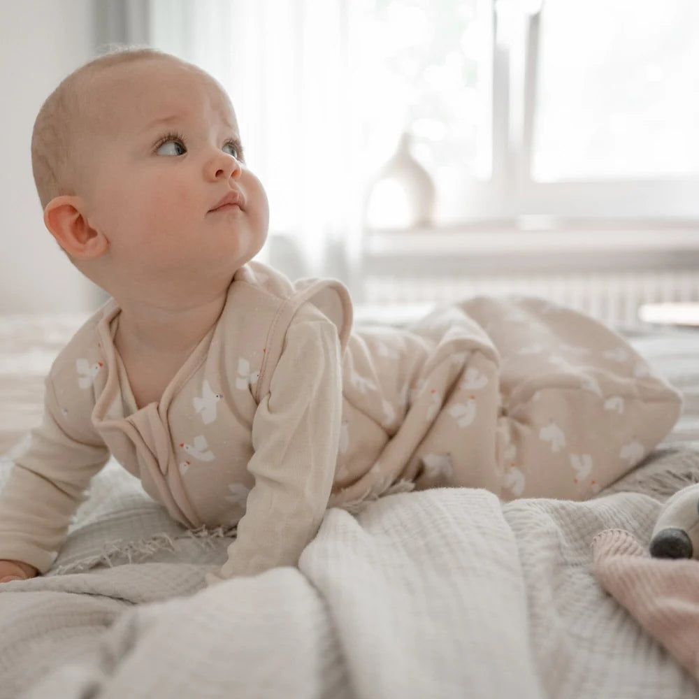 Baby trägt den beigen Emma & Noah Kugelschlafsack mit weissem Vogelprint, erhältlich im Bärechind in Winterthur, Zürich, Schweiz.