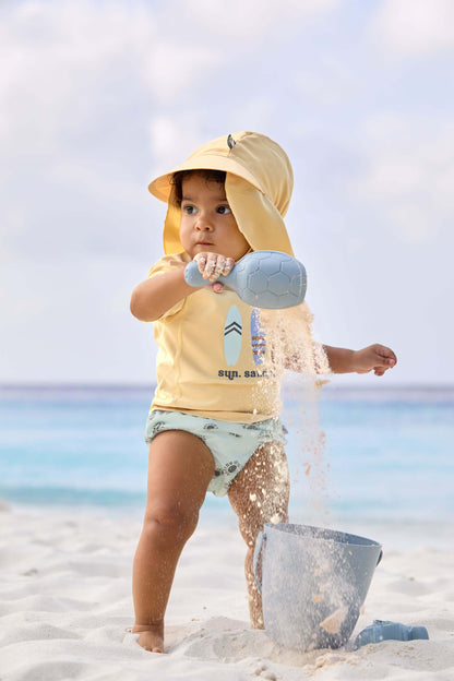 Sonnenhut von Lässig für Babys in Gelb – mit UV-Schutz 80 & langem Nackenschutz, Angezogen an Strand.