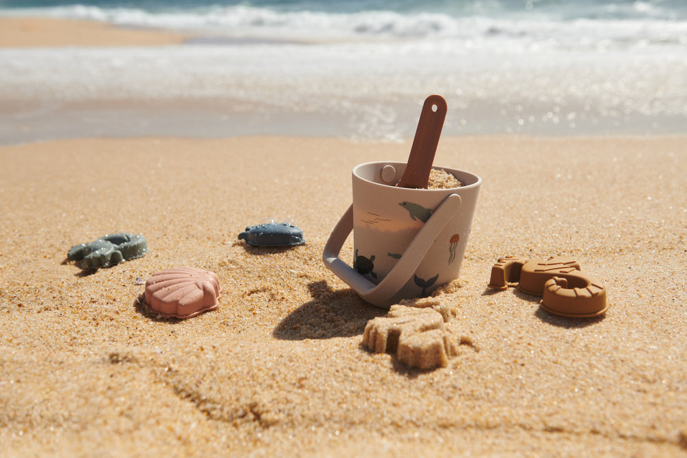 Liewood Gilma Strandeimer-Set in Sea Creature Sandy am Strand im Einsatz. Eimer mit Meeresmotiven, Schaufel und Sandformen für kreativen Spielspass im Sand. Erhältlich in Winterthur, Zürich, Schweiz.