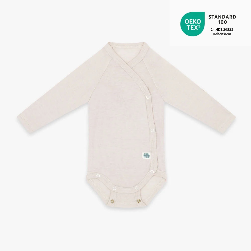 Baby trägt den beigen Merino Wickelbody von Emma & Noah als weiche erste Kleidungsschicht, erhältlich im Bärechind in Winterthur