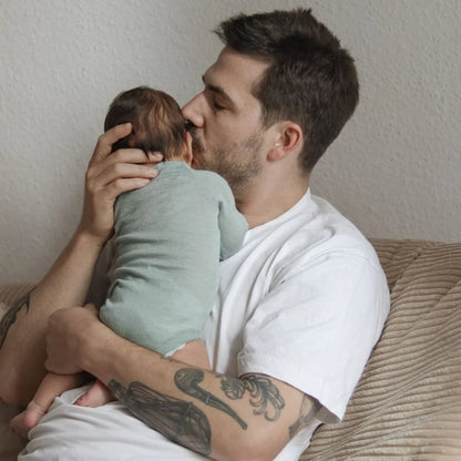 Baby im mintfarbenen Emma & Noah Merino Wickelbody auf dem Arm seines Vaters, erhältlich im Bärechind in Winterthur und online in der Schweiz.