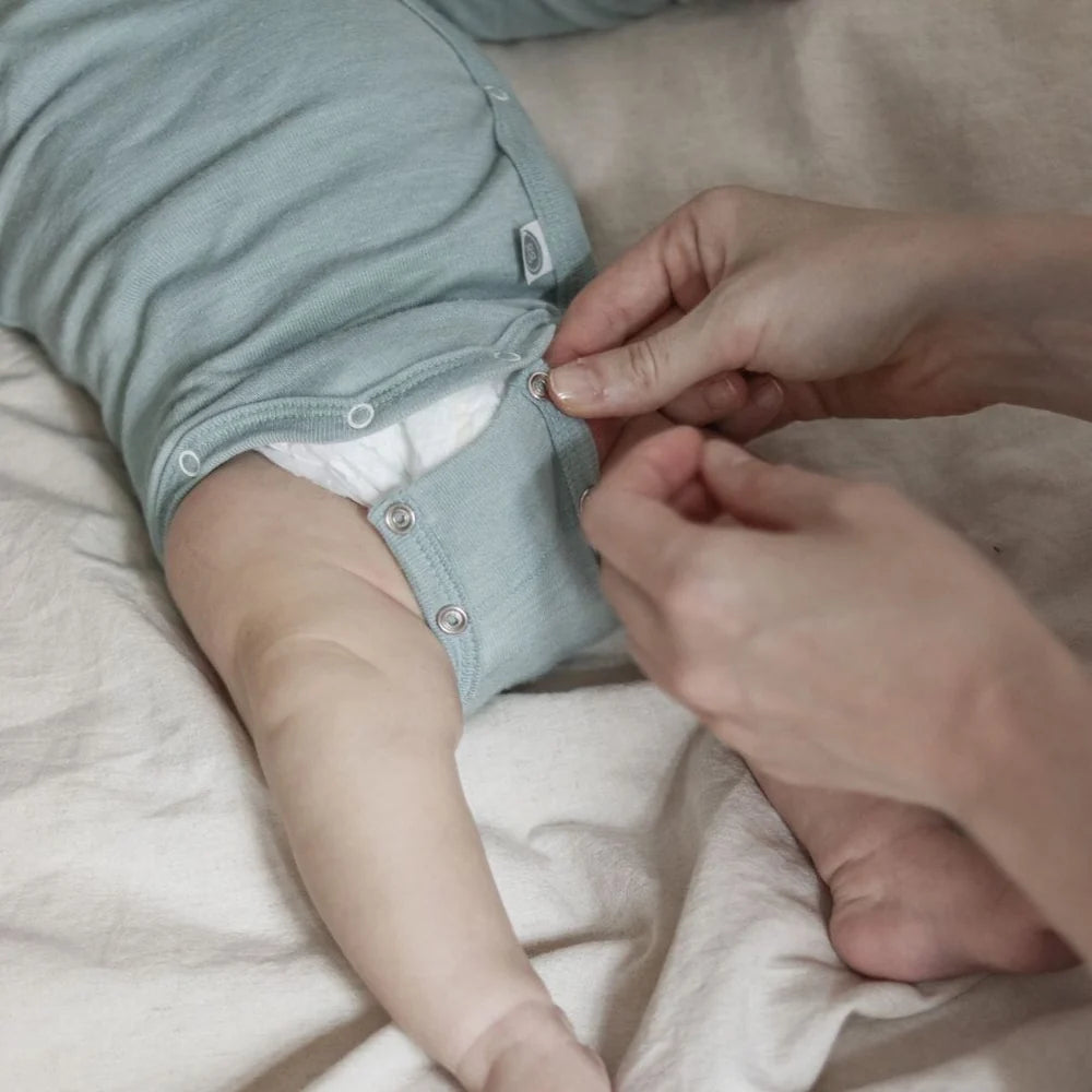 Detail des Emma & Noah Merino Wickelbodys in Mint beim Wickeln eines Babys, erhältlich im Bärechind in Winterthur