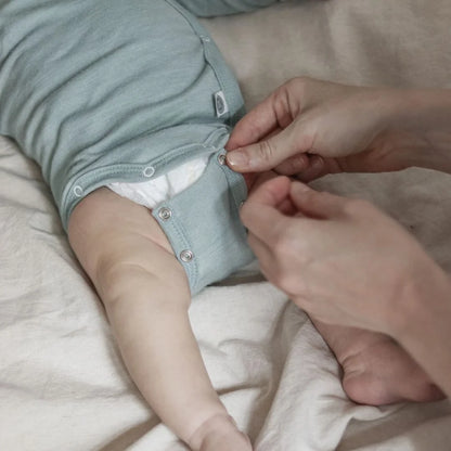 Detail des Emma & Noah Merino Wickelbodys in Mint beim Wickeln eines Babys, erhältlich im Bärechind in Winterthur
