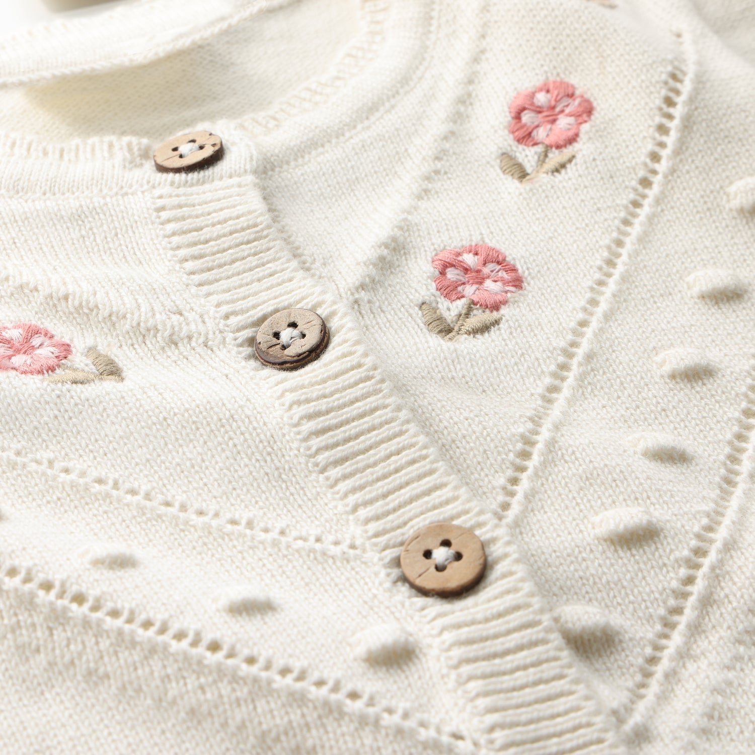 Detailaufnahme Stickerei und Knöpfe der Minymo Strickjacke aus Bio-Baumwolle im Bärechind Winterthur, Zürich, Schweiz