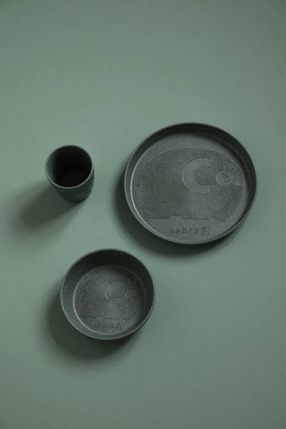 MUMS-Geschirrset in Dunkelgrün als Flatlay auf einem hellgrünen Hintergrund angeordnet