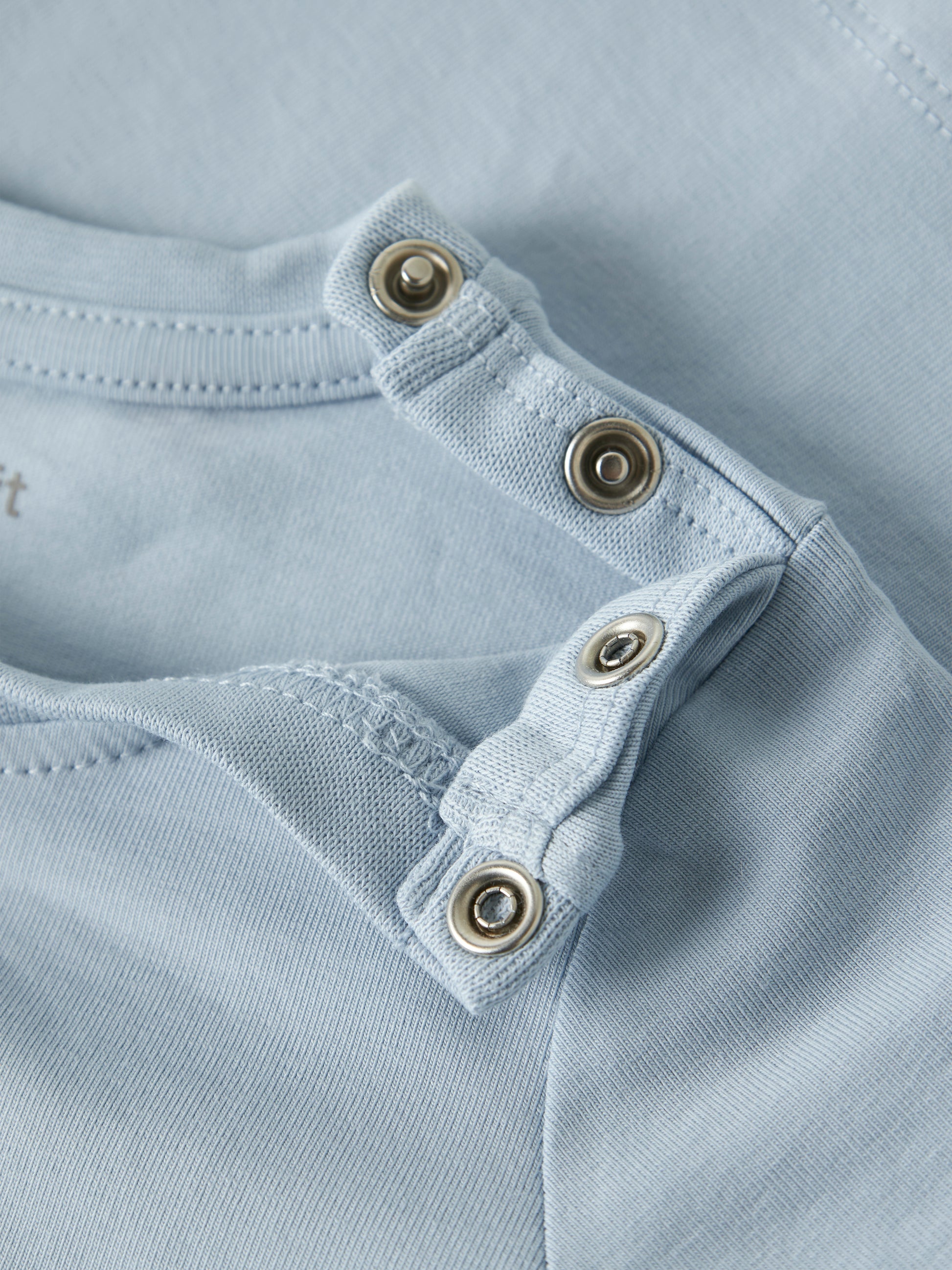 Detailaufnahme der Schulterdruckknöpfe am hellblauen Name It Kinder T-Shirt mit Löwenmotiv im Bärechind Winterthur