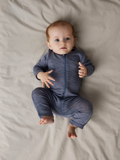 Ein Baby liegt in einem blauen Merino-Schlafanzug von Name It auf dem Bett.