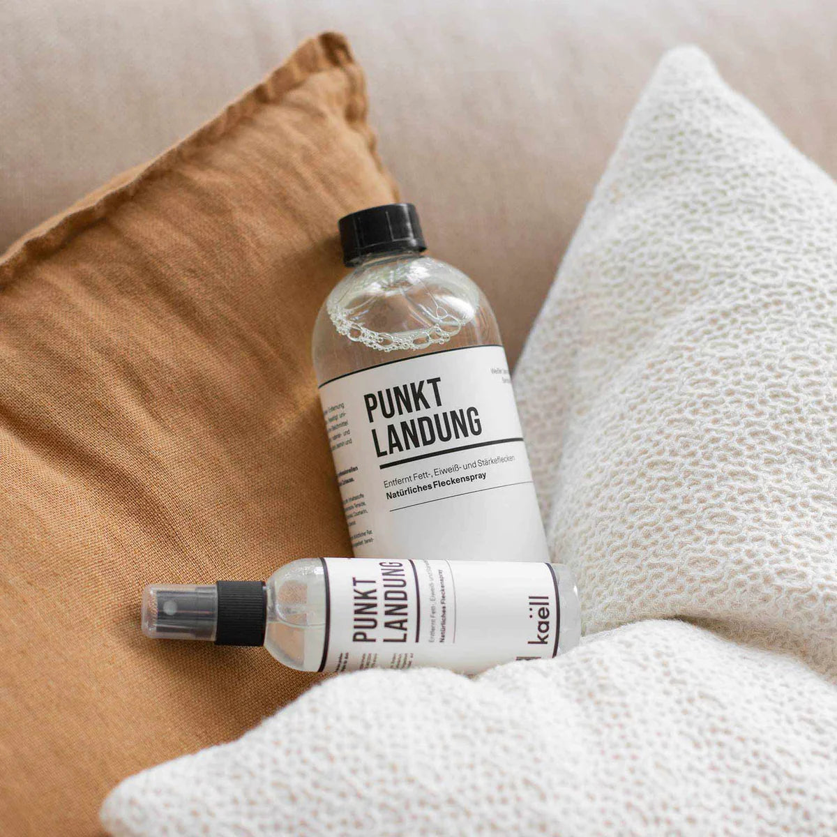 Punktlandung Pflegespray von Kaëll in 500ml und 50ml Flaschen, dargestellt auf einem weichen Kissen, geeignet für die schonende Entfernung von Fett-, Eiweiß- und Stärkeflecken