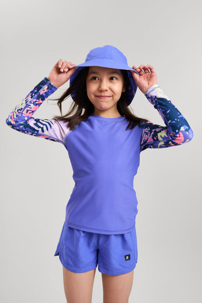 Kind trägt Reima Nauru Badeshorts in Lila – ideal für Sommer, Strand und Wasser