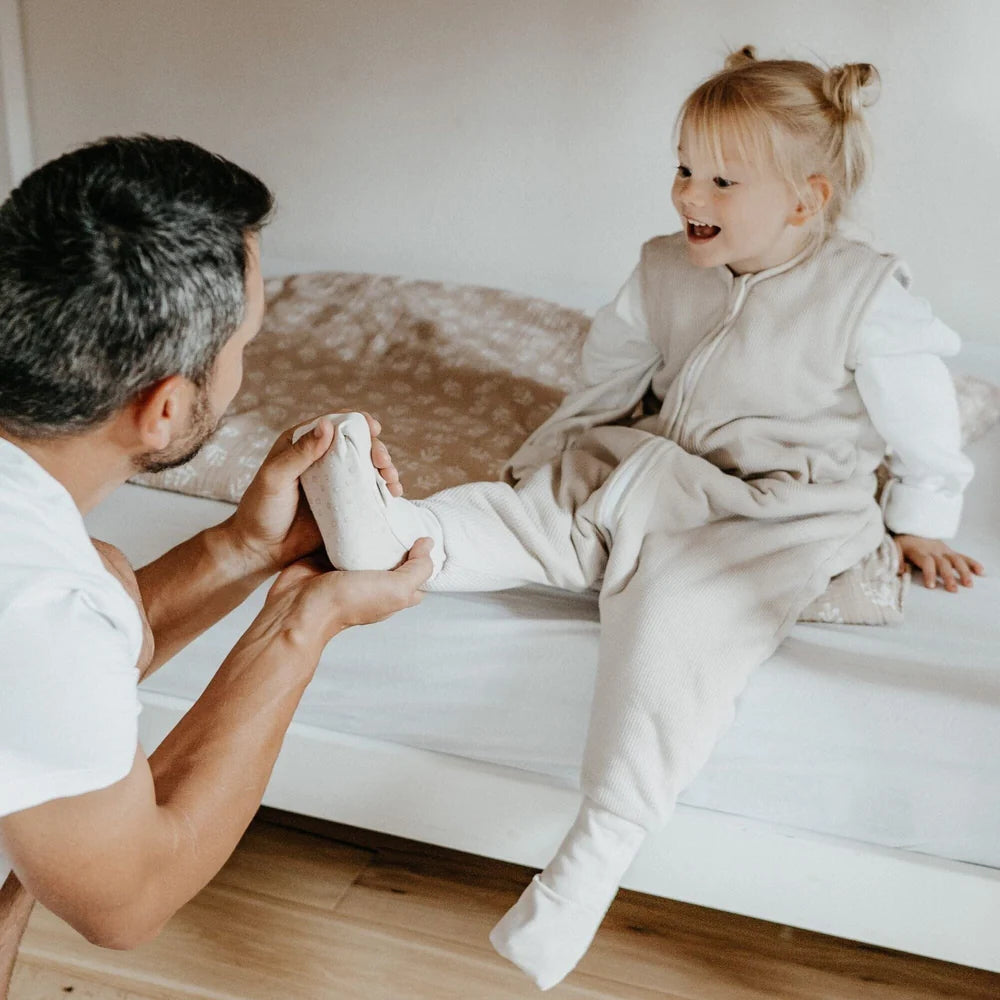 Kind im beigen Emma & Noah Schlafsack mit Füssen für kühle Nächte, erhältlich im Bärechind in Winterthur bei Zürich und online in der Schweiz.