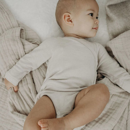 Emma & Noah Merino Wickelbody in Beige beim Anziehen eines Babys, erhältlich im Bärechind in Winterthur