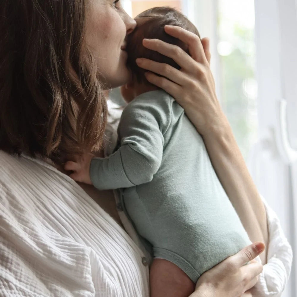 Baby trägt den mintfarbenen Wickelbody aus Merinowolle von Emma & Noah